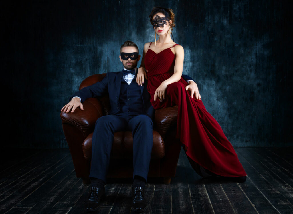 Woman in red dress sitting on sofa with gentleman in suit on dark background